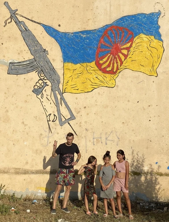 Давид Чичкан на тлі стінопису з українсько-ромським прапором, створеному у
співавторстві з Микитою Кравцовим в мікрорайоні Радванка, Ужгород, 2022