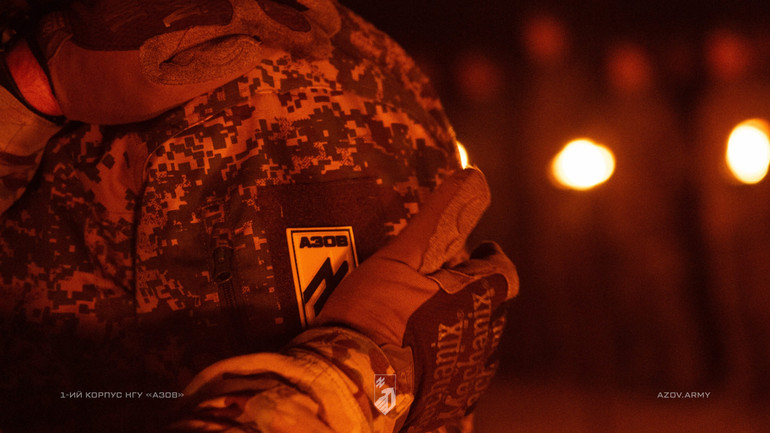 Військовий у пікселі з нашивкою Азов у темряві при світлі вогнів.