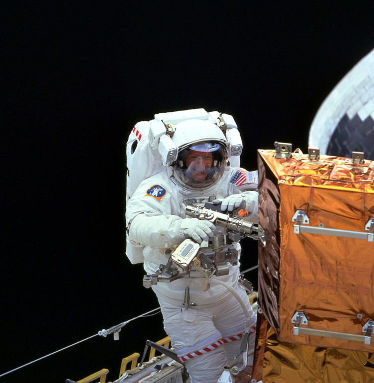 An astronaut uses the Pistol Grip Tool in outer space