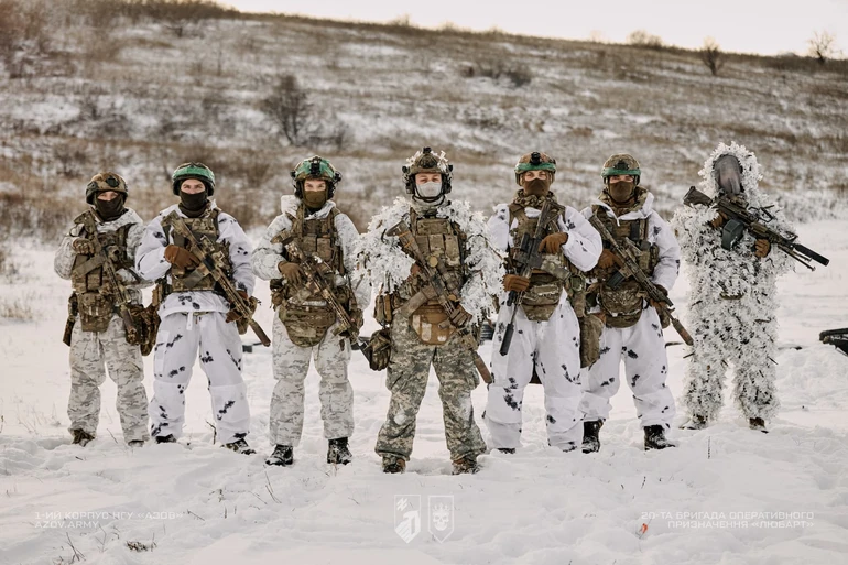 Група військових у зимових маскувальних костюмах зі зброєю стоїть у строю на засніженій місцевості під час навчань.